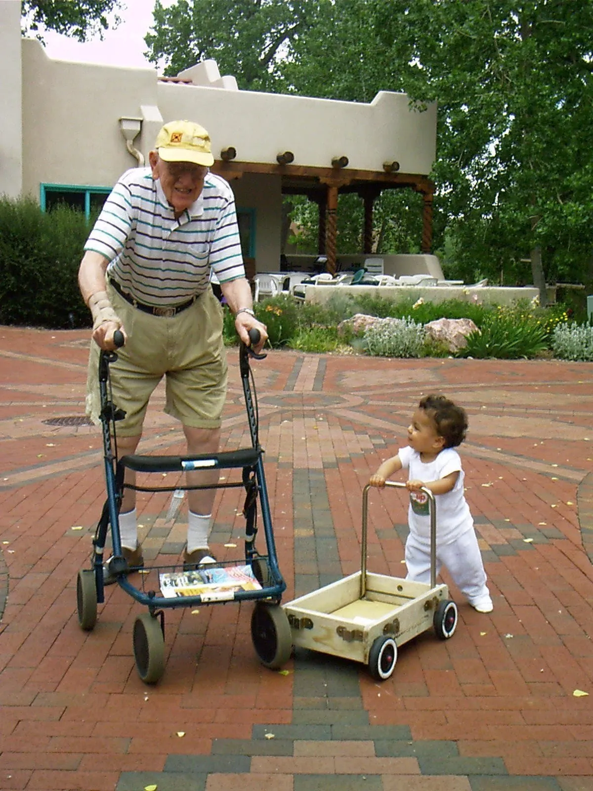 Elderly resident with walker and toddler with push toy walking together on brick plaza