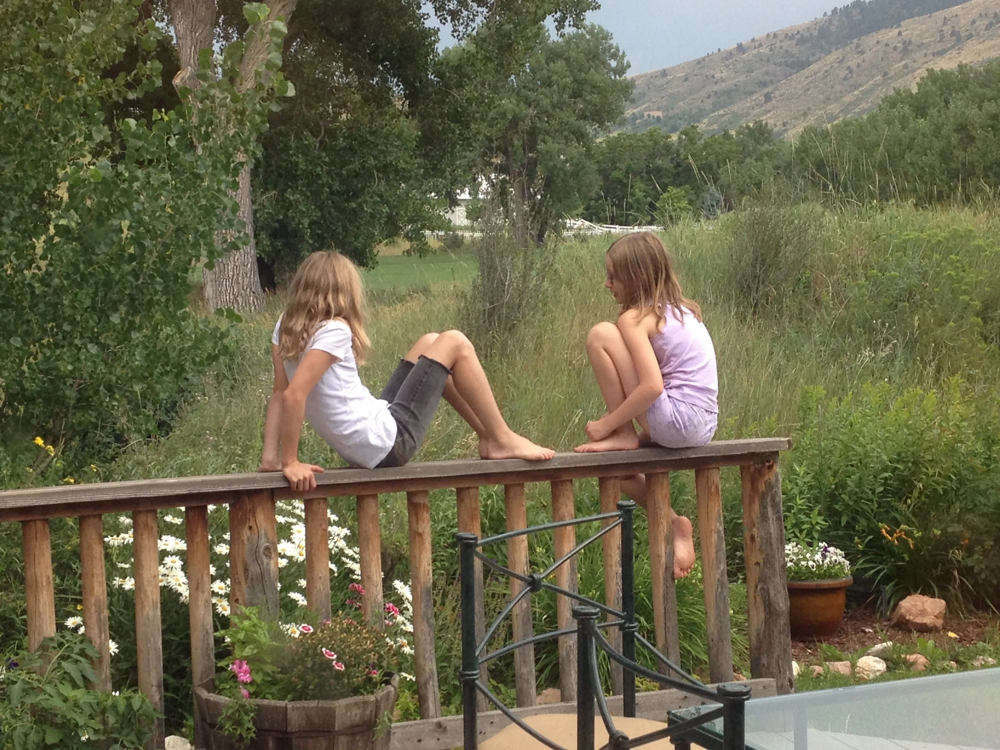Two children sitting on a wooden bridge overlooking the community garden with mountains in the background